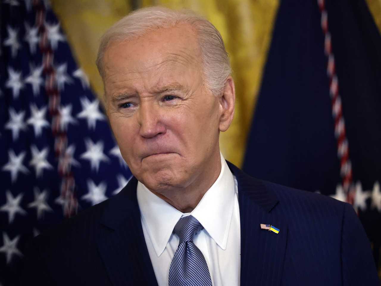 A tight-lipped President Biden with flags behind him.