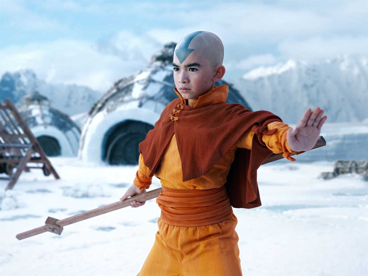 Aang holds out a hand and his staff in front of a snowy backdrop.