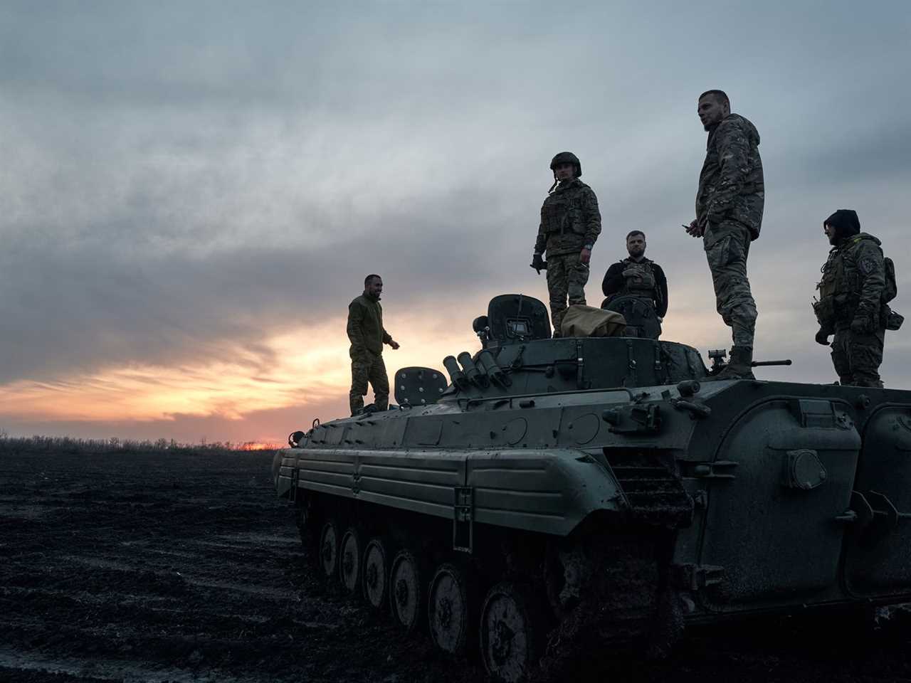 Soldiers standing on a tank in the sunset.