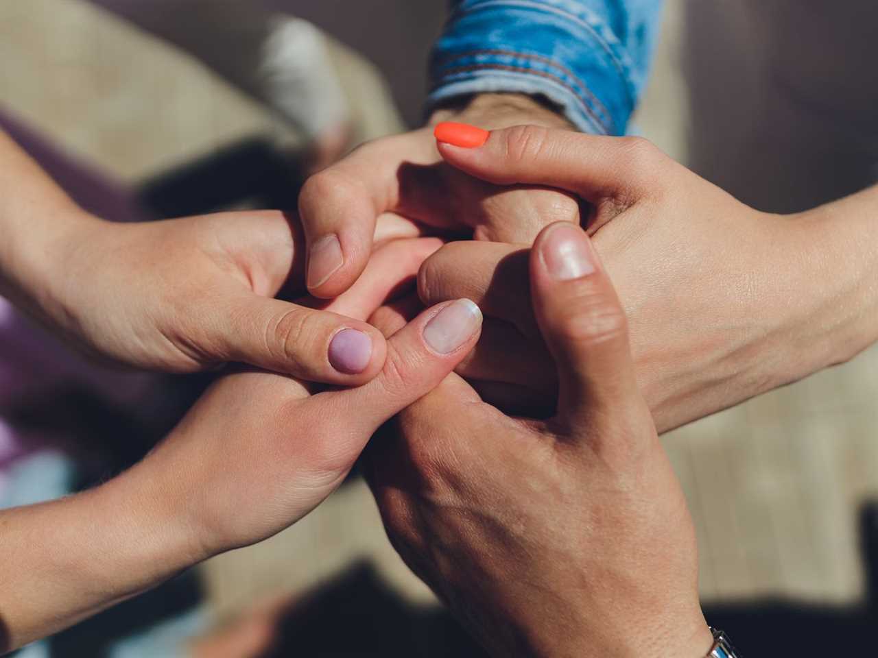 Two men and three women holding hands on a table implying a polyamory relationship or love triangle.