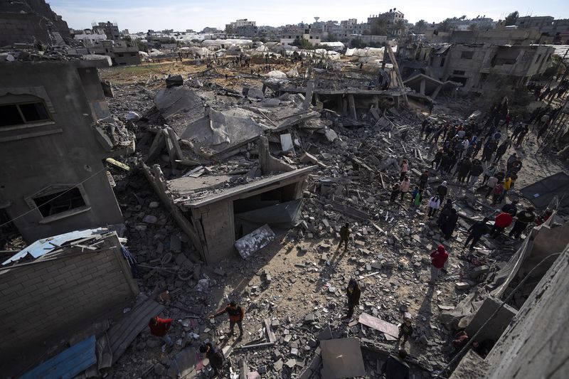 People stand in the rubble of buildings that have been bombed and destroyed.