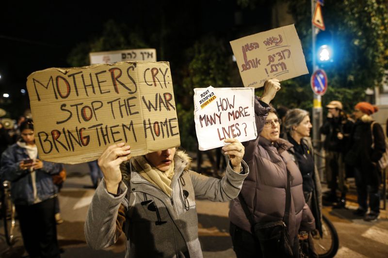 People hold signs saying “mothers cry stop the war bring them home” and “how many more lives.”