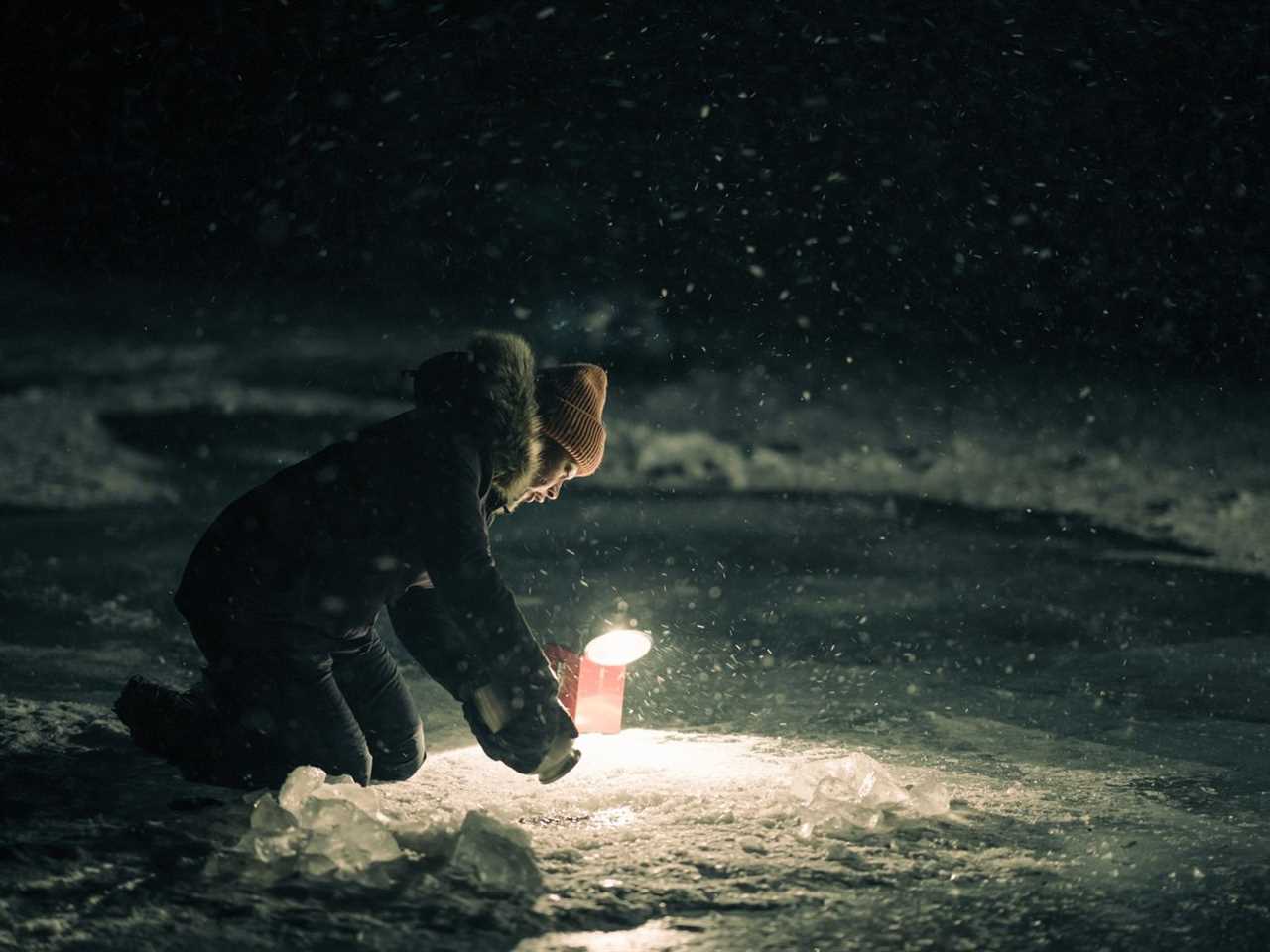 A woman holds a flashlight while kneeling, the light showing ice-covered water.