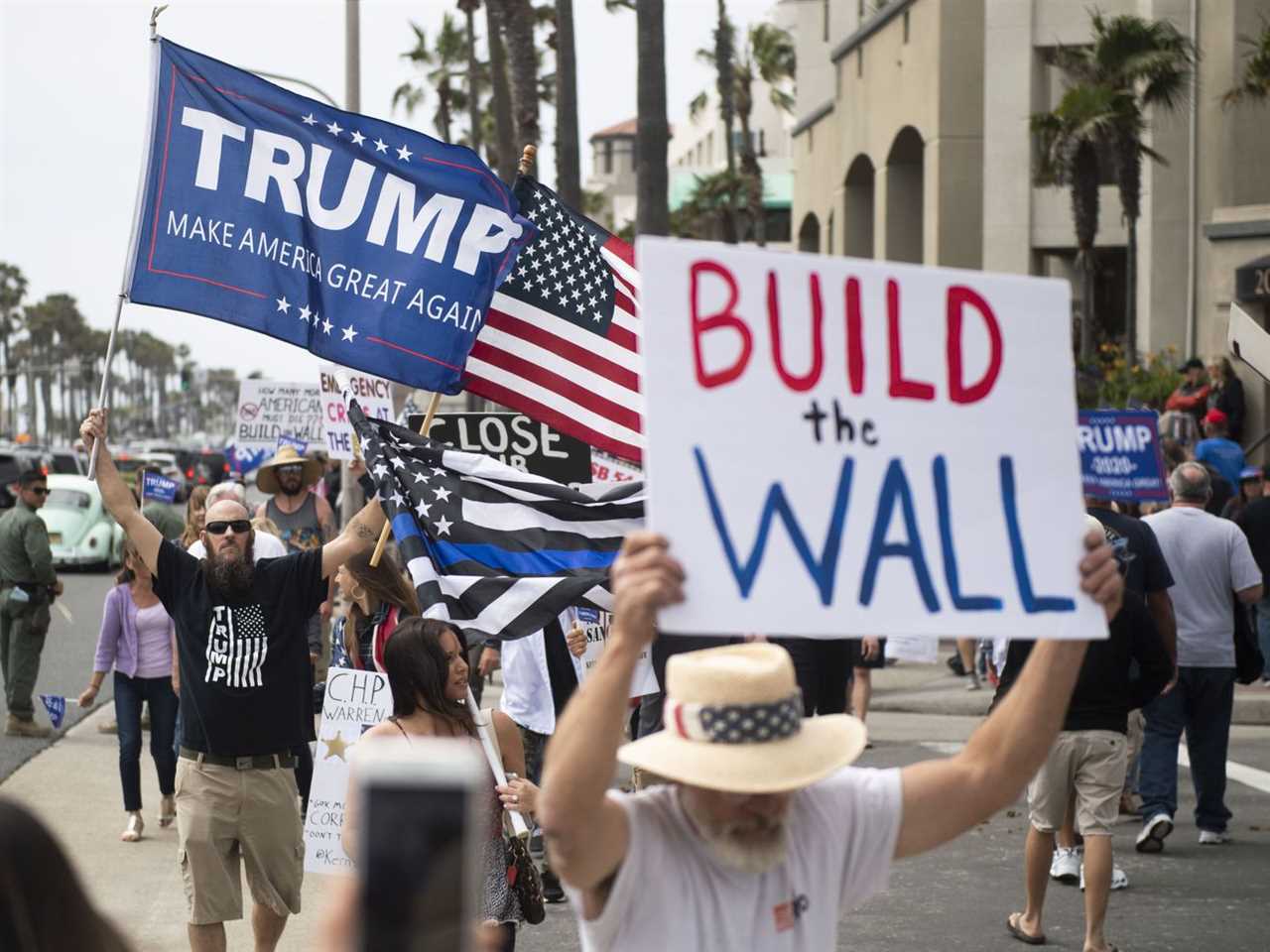 Anti-immigration protesters in Huntington Beach, California, hold a Trump flag and a sign saying “Build the Wall.”