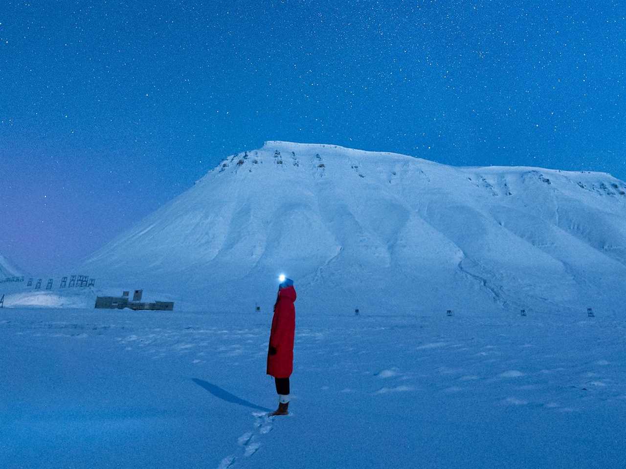 A woman in a red coat stands in a dark blue snowy landscape.