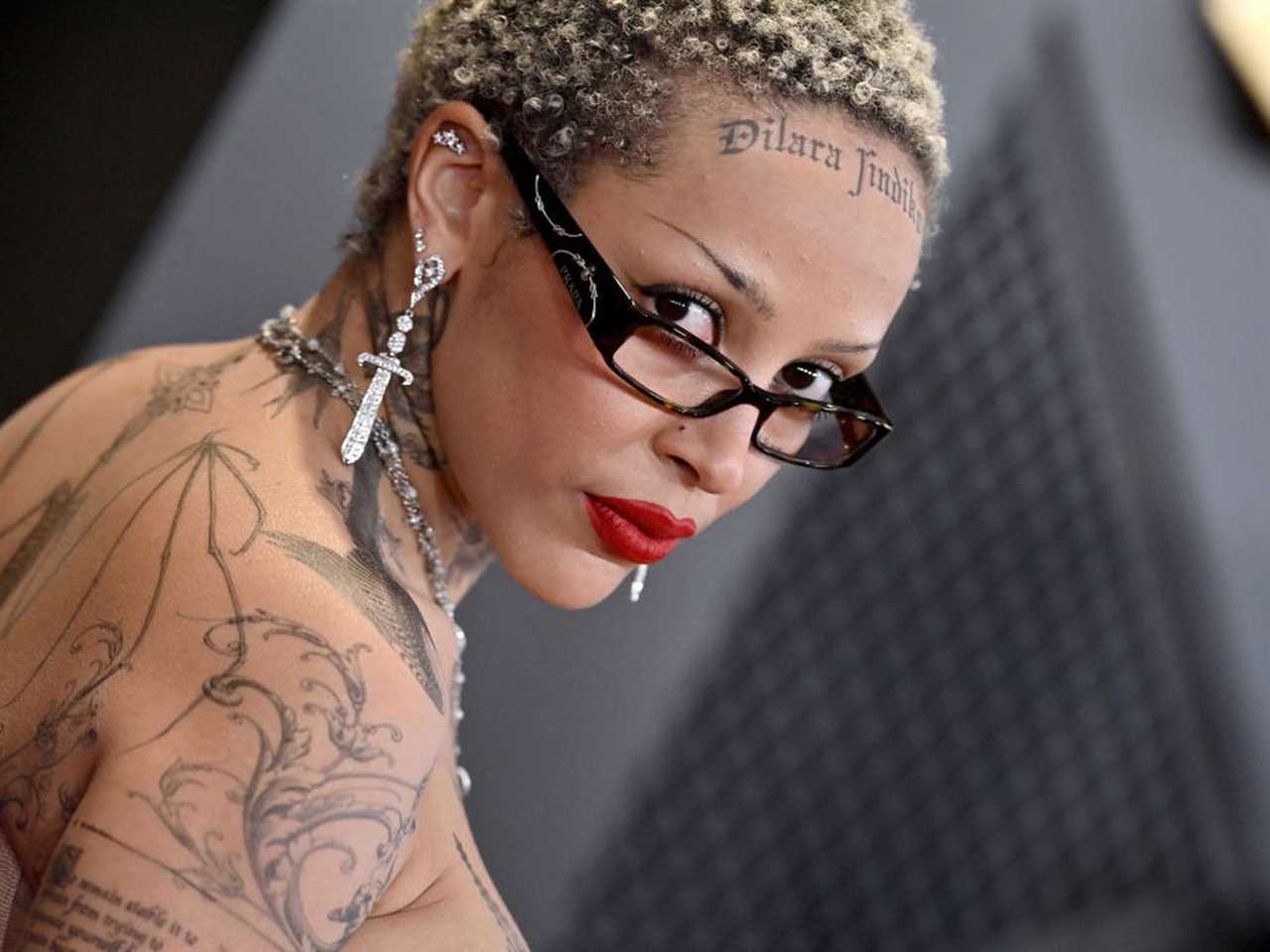 A woman with tattooed shoulders and short hair wearing tiny eyeglasses.