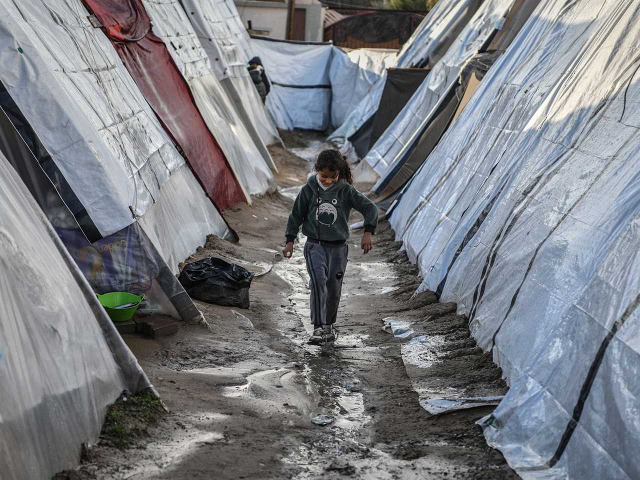 A child walks over muddy ground between rows of tents.