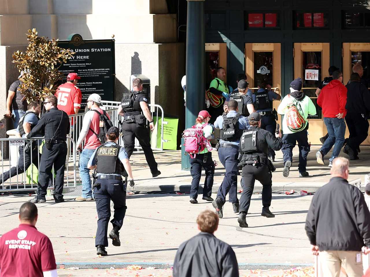 Pedestrians and police officers running toward a city building.